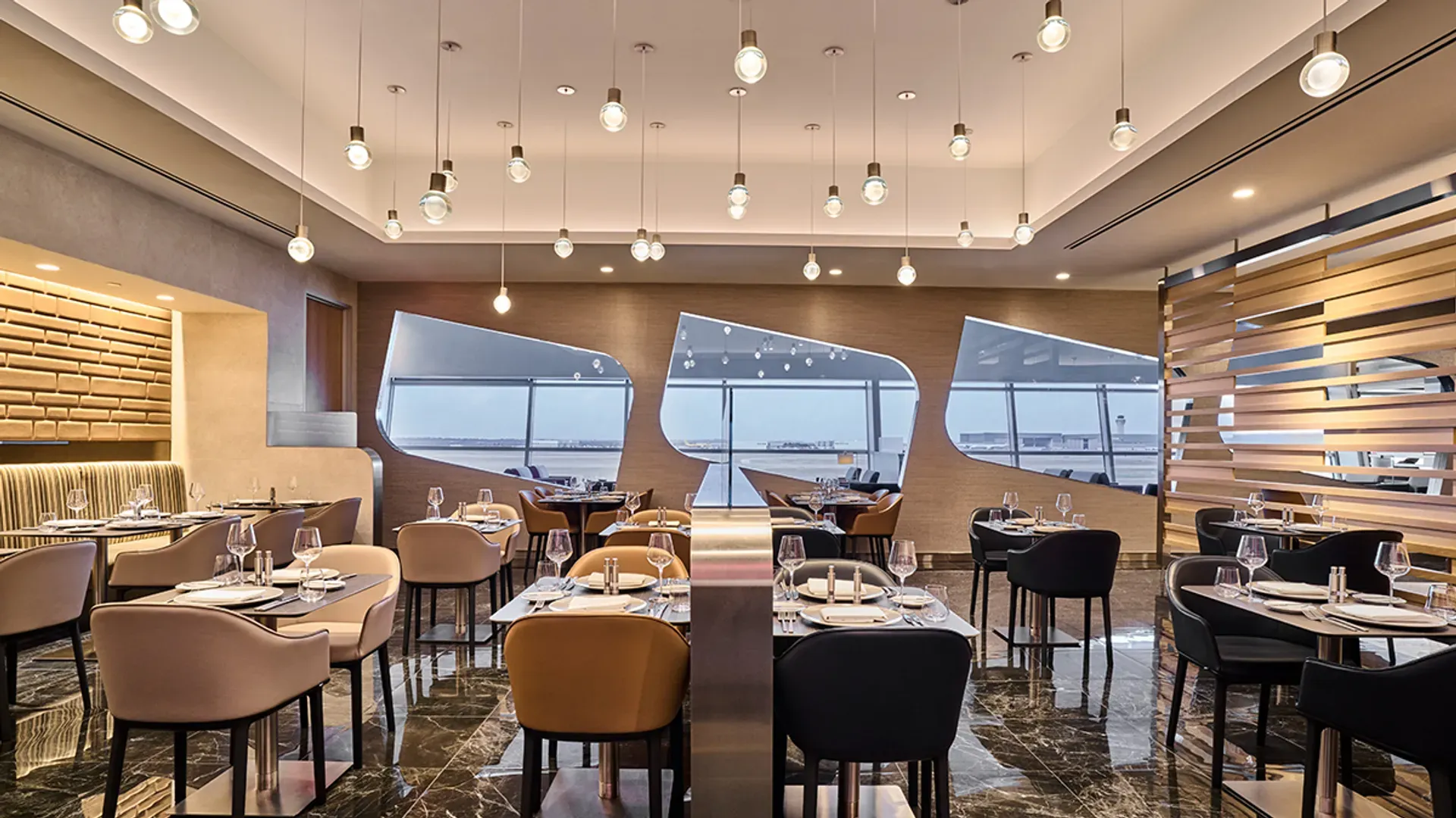 Salle de restaurant avec tables dressées, verres à vin, boiseries et grandes fenêtres dans un salon Flagship d'American Airlines