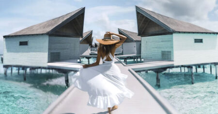 A woman walking along a boardwalk between overwater bungalows in a tropical setting