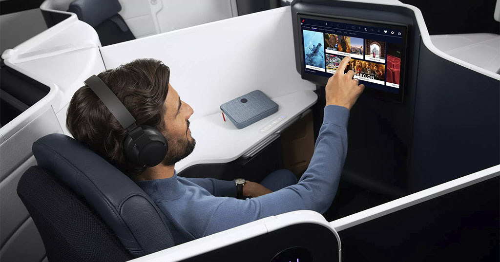 A person wearing headphones in an airplane seat, using a touchscreen for in-flight entertainment
