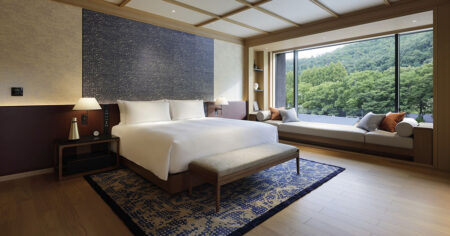 A spacious, elegant bedroom with a large bed and a window seat providing a view of lush greenery outside