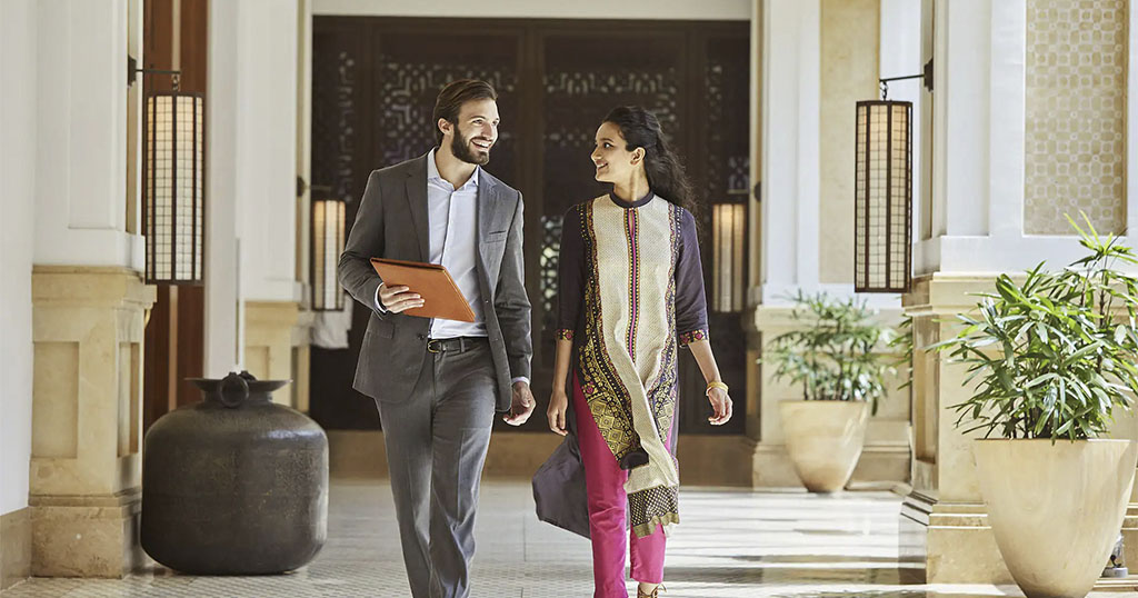 A man and woman walking and smiling in a stylish, well-lit corridor with decorative elements and plants