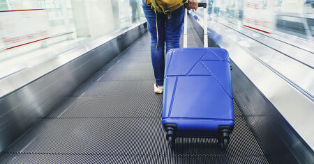 A traveler pulling a blue suitcase on an airport moving walkway