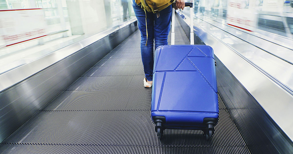 A traveler pulling a blue suitcase on an airport moving walkway