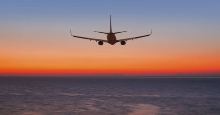 An airplane flies into a vibrant sunset over the ocean