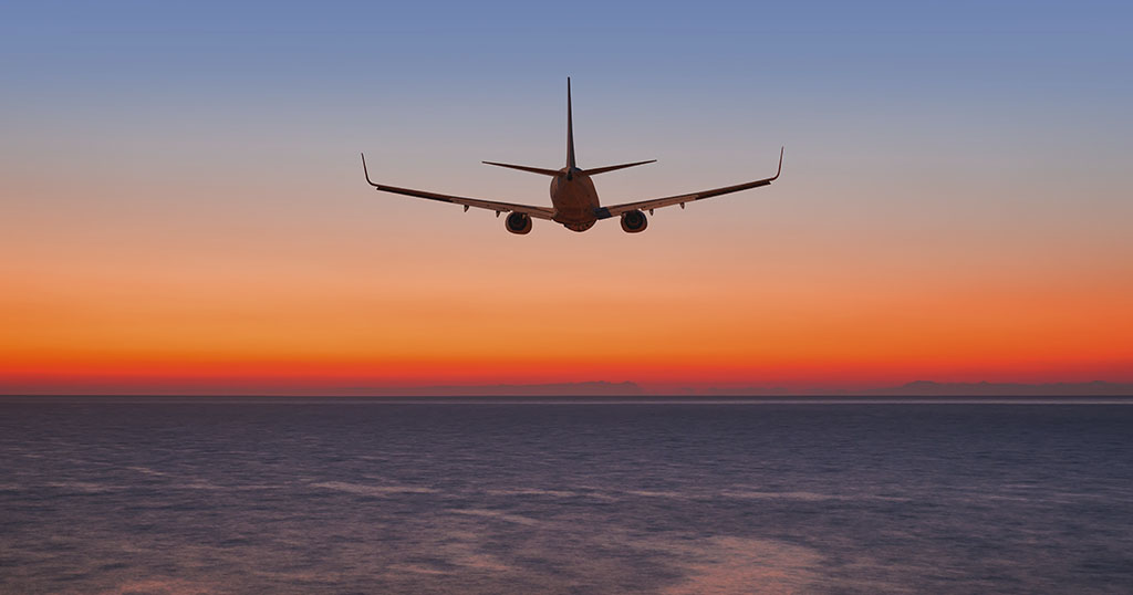 An airplane flies into a vibrant sunset over the ocean