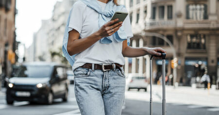 A person walking in the city, checking their phone and pulling a suitcase