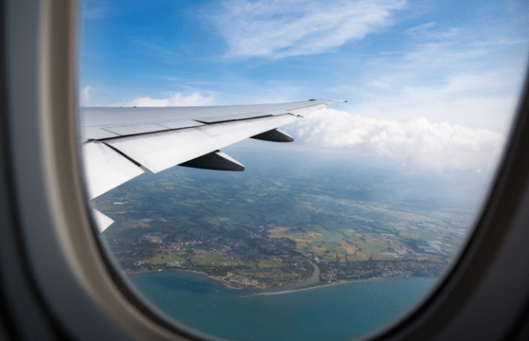 airplane wing out the window with water, clouds, and greenery